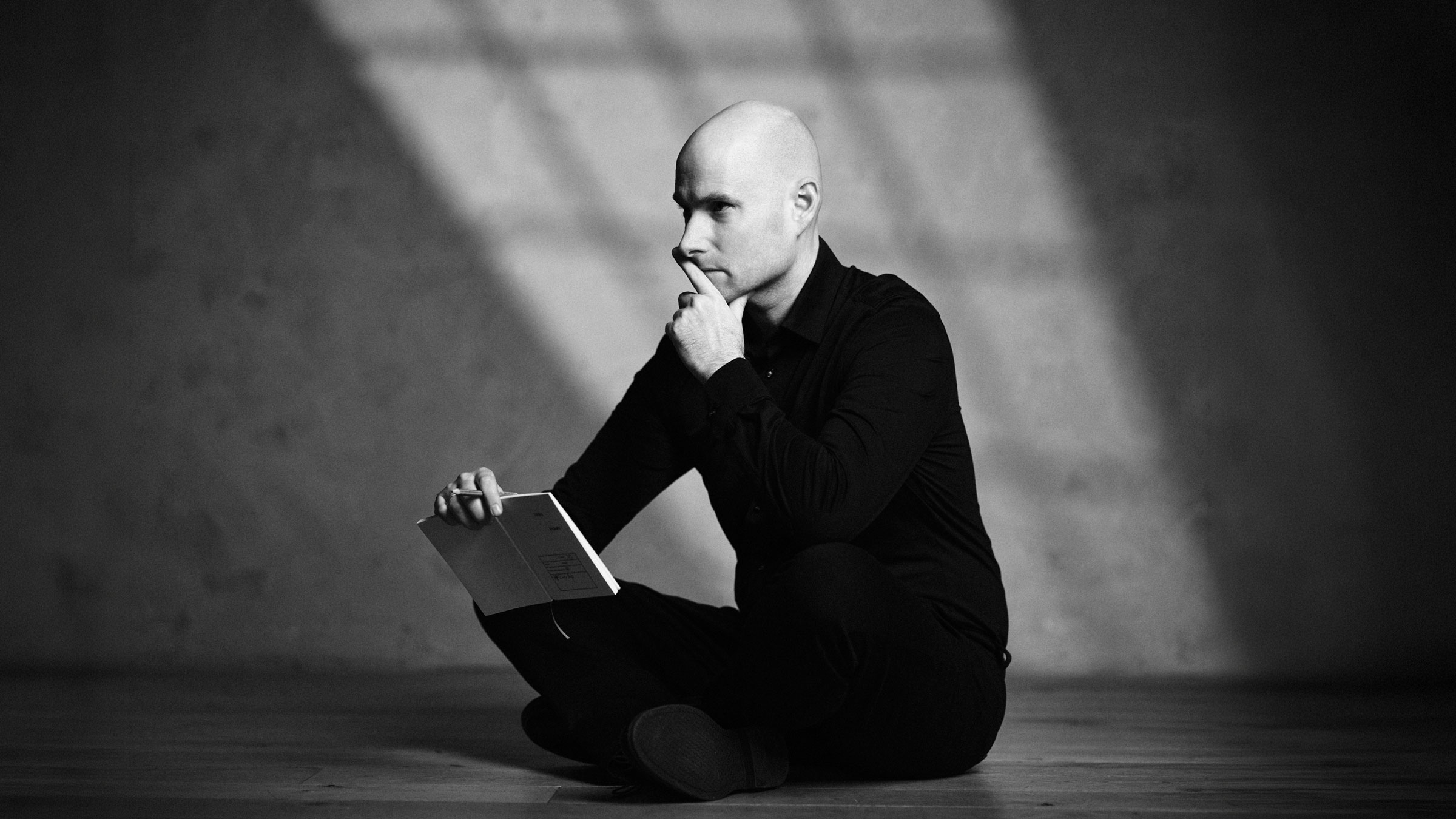 Michael Wax im Schneidersitz am Boden sitzend mit einem Buch in der Hand und der anderen am Kinn