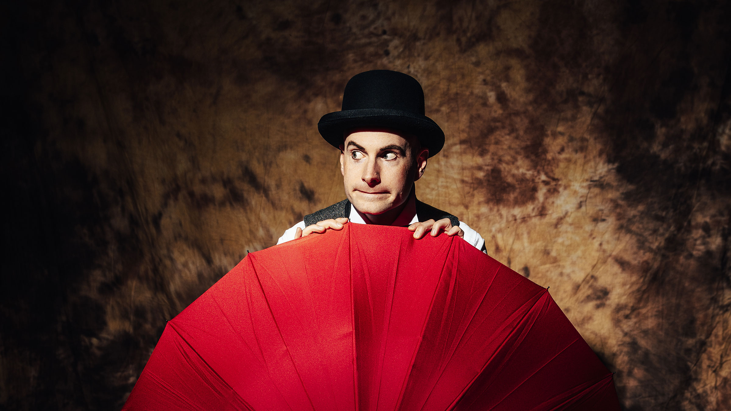 Michael Wax with a melon on his head, peeking out from behind a red umbrella